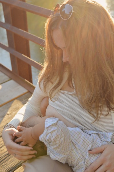 new mom woman sitting outdoors on dock in summertime breastfeeding her baby